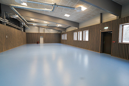 Sporthall med blått golv och träpanel på väggarna.