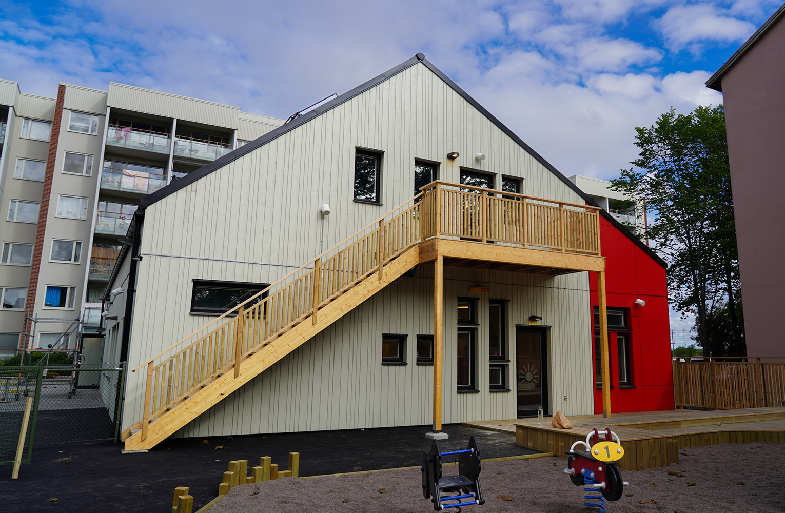 Leksaker i sandlådan framför vit gavel på hus med två våningar.