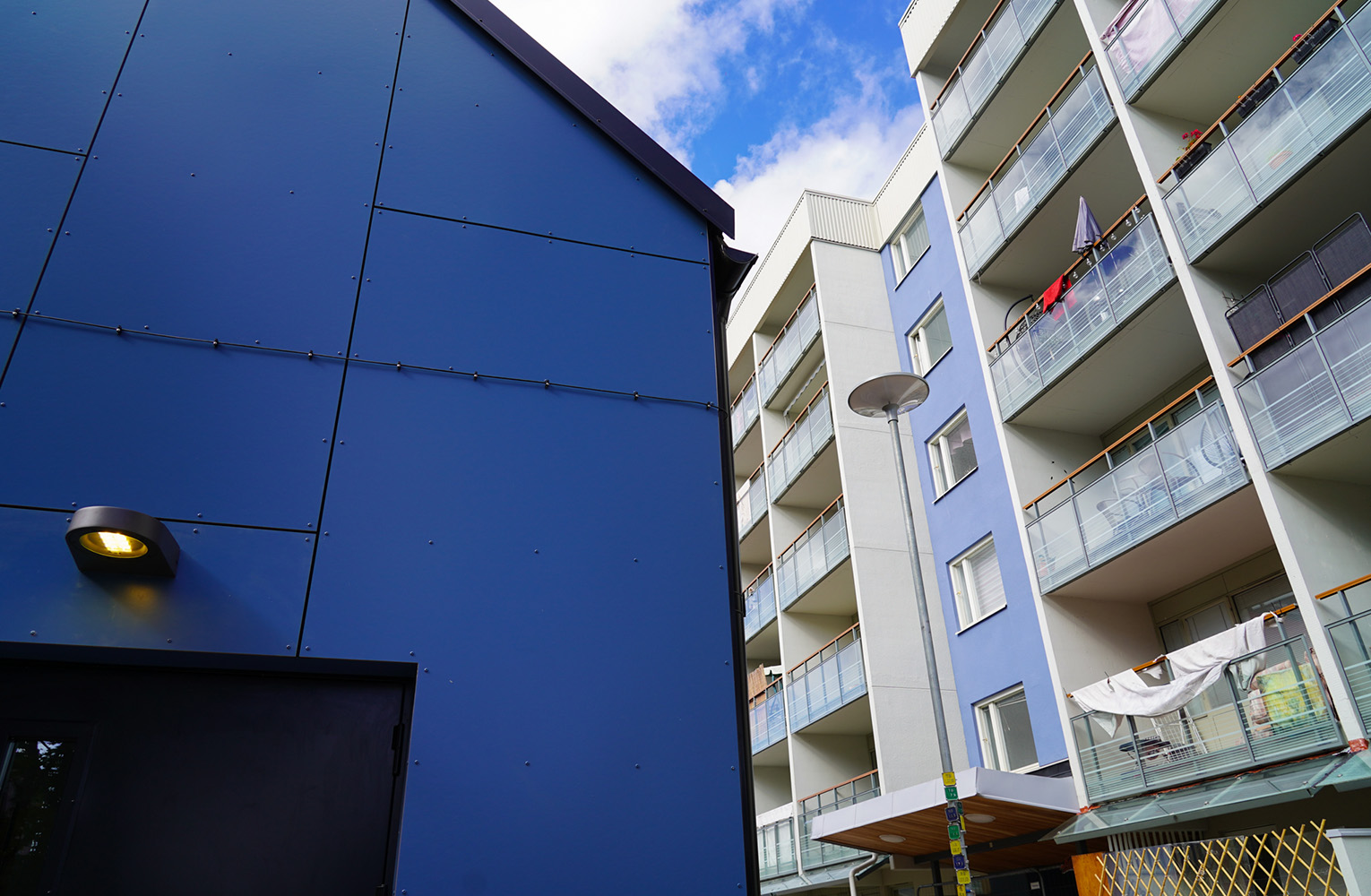 Del av blå gavel på hus, framför balkonger på flervåningshus.