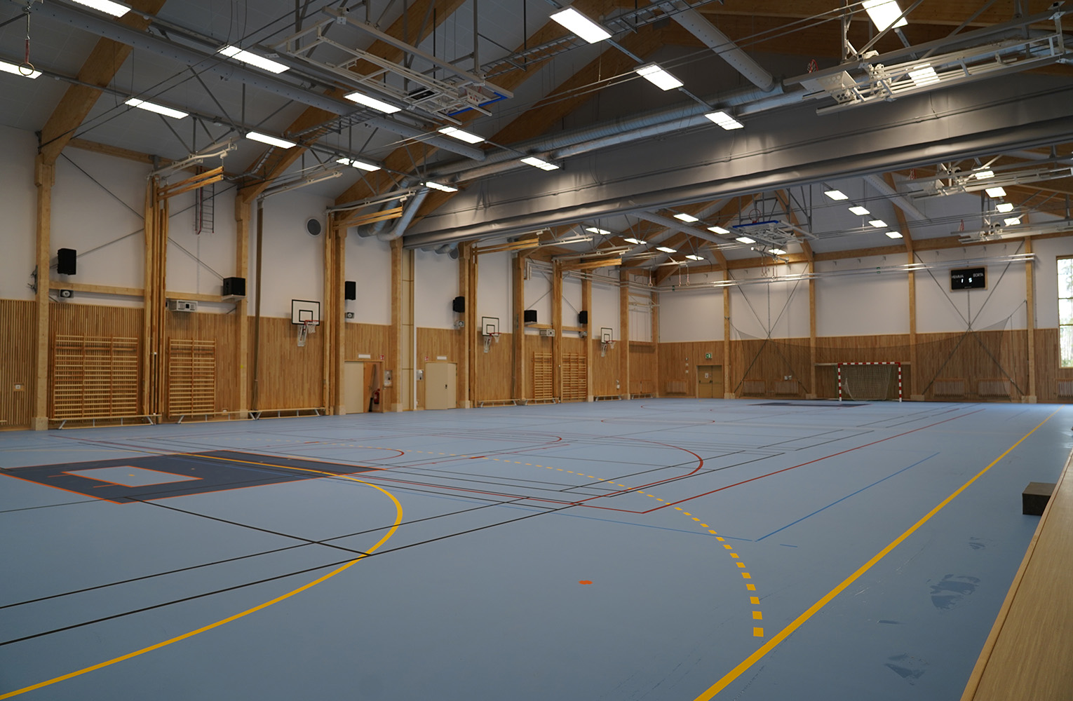 Idrottshall med ljusblått golv, linjemarkeringar och ribbstolar.