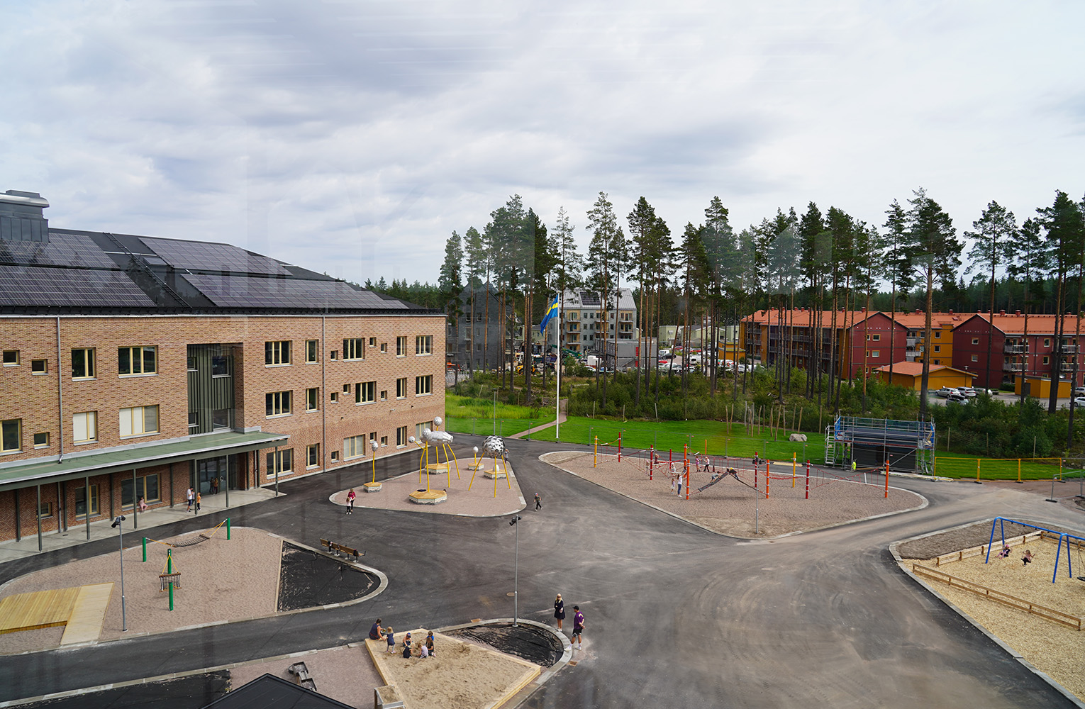 Utsikt över skolgård, asfalterad yta med områden i sand är lekredskap finns.