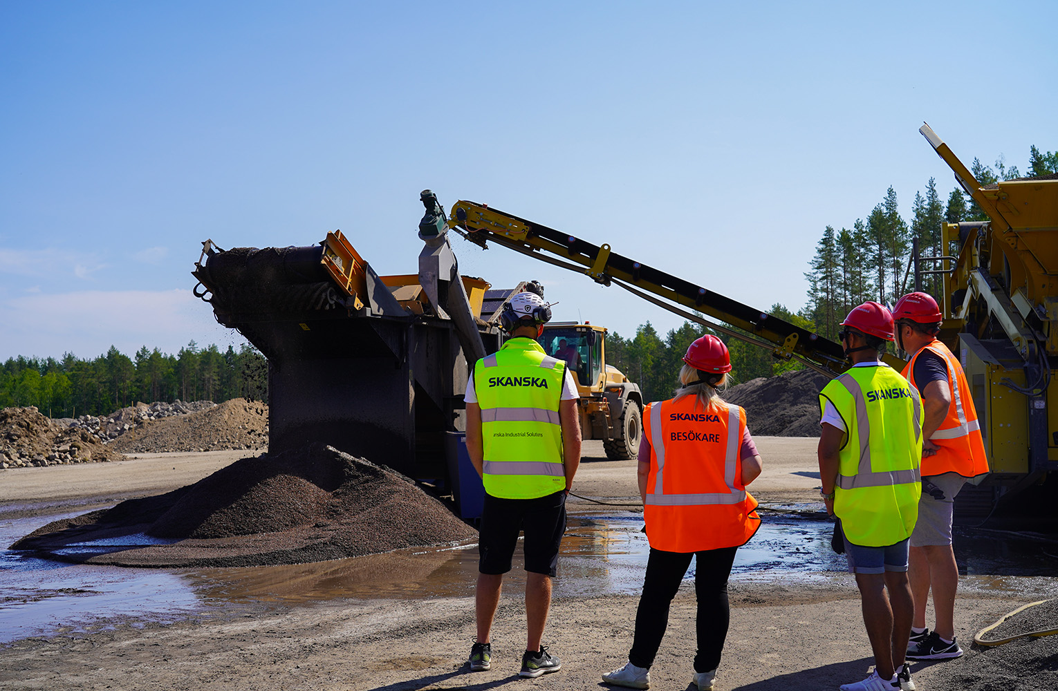 Fyra personer med skyddskläder övervakar maskiner som utför sandtvätt.