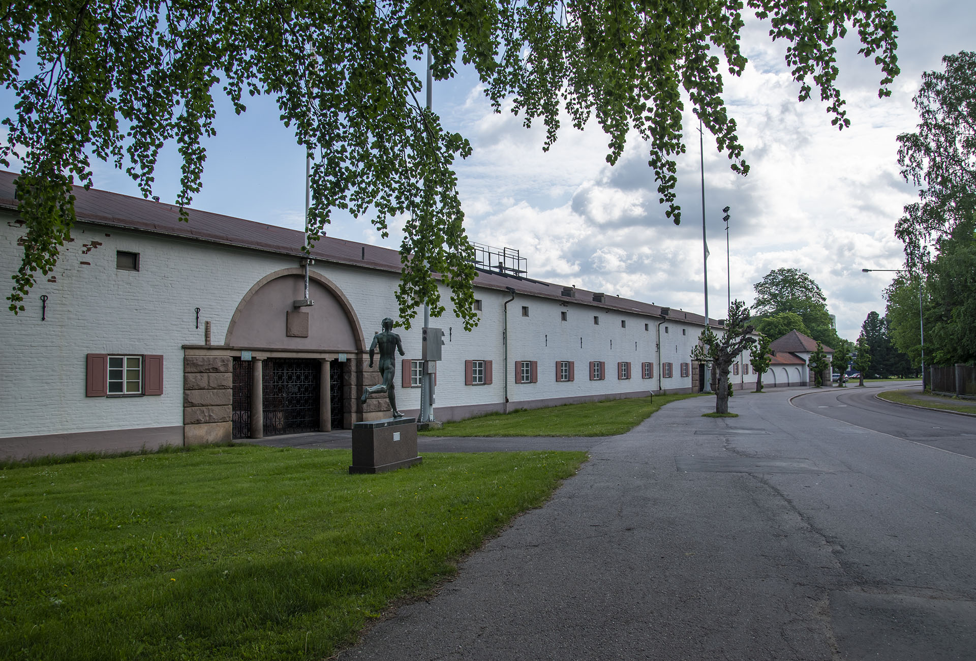 Vit låg byggnad följer asfalterad väg, staty på person som springer.