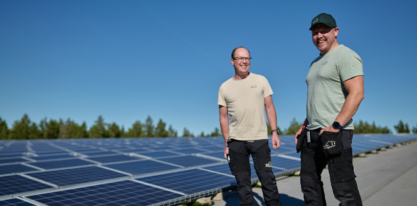 Två män står bredvid varandra framför en solpanel.